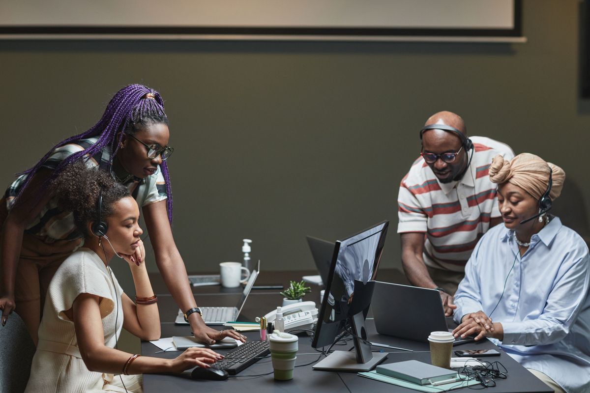Four young professionals, women and men, working together at computers around a shared desk